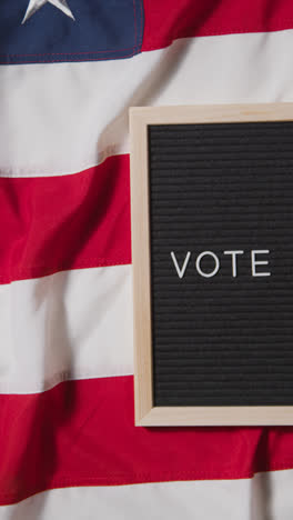 Vertical-Video-Of-Sign-Reading-Vote-Lying-On-US-Stars-And-Stripes-Flag-For-American-Election-2024-1